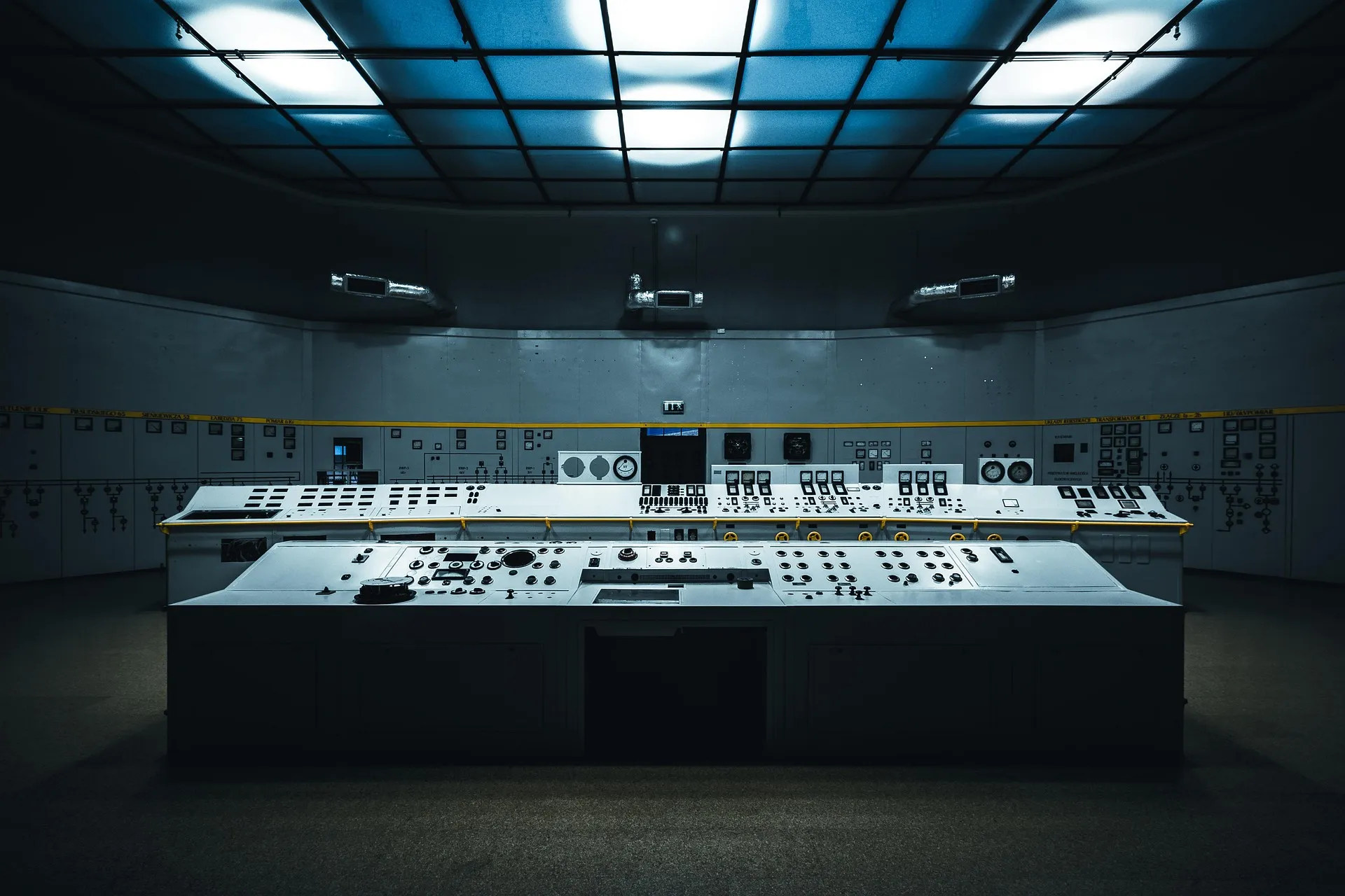 A dimly lit control room: a long console of switches and dials, with schematic panels lining the wall behind